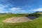 Golf course with sand bunker and vibrant fairway under blue sky on a sunny day