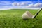 Golfball and stick on green grass golf course, blue cloudy sky background