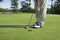 Golfer taps in with putter on green with trees near a lake