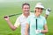 Golfing couple smiling at camera holding clubs