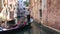 Gondola with tourists floats on a narrow urban channel. Venice