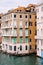 A gondola with tourists is sailing along the Grand Canal amid the facades of Venetian houses standing on the water in