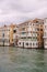 A gondola with tourists is sailing along the Grand Canal amid the facades of Venetian houses standing on the water in