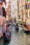 Gondolier rowing gondola with tourists on narrow canal in Venice