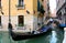 Gondolier rowing in gondola on Venetian canal surrounded by picturesque facades of old buildings next to the Cavalletto Hotel