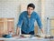 Good looking Asian carpenter working for DIY jobs in carpenter room with several kinds of woods and types of equipment