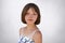 Good-looking brunette kid with freckles and short hair posing against white concrete wall dressed in white dress. Little child wit