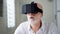 Good-looking handsome senior man in white using VR 360 glasses at home. Active modern elderly people