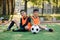 Good-looking joyful teen football players resting on the artificial grass covering of soccer field after training.