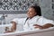 Good-looking relaxed dark-skinned mixed race woman in bathrobe sitting in bathtub having rest