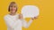 Good looking senior lady holding blank speech bubble with free space and smiling to camera, orange studio background