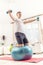 Good looking young male exercising with Swiss ball and dumbbells at home. Arms extended, kneeling on a fitball, holding a position