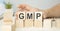 Good Manufacturing Practice. GMP the word on wooden cubes, cubes stand on a reflective surface, in the background