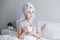 Good morning and skin care concept - portrait of woman sitting in bed with facial mask and cup of coffee