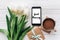 good morning text sign on phone screen and stylish gift and tulips and coffee on white wooden rustic background. flat lay with fl