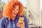 Good news. Happy young woman with red curly hair, surprised looking her mobile phone. Good news. Isolated city background.