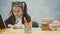 A good schoolgirl sits at the table on a gray background. During this, he writes homework while looking at the book