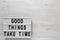 `Good things take time` words on a lightbox on a white wooden surface, top view. Overhead, from above, flat lay. Copy space