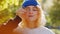 Goofy funny European young adult woman with blond, curly hair under a blue hat blinking her eyes and covering one eye