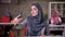 Gorgeous arab woman is gray hijam takes selfies on her smartphone while sitting at workplace, colleagues girls on