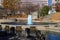 A gorgeous autumn landscape in the park with a still green lake and a water fountain in the center of the lake