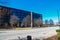 A gorgeous black and glass office buildings on a street surrounded by bare winter trees and a tall rusty smoke stack