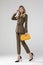 Gorgeous blonde model posing in olive suit and chic yellow handbag.