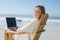 Gorgeous blonde sitting on deck chair using laptop on beach