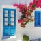 A gorgeous bougainvellia on e white house wall with blue windows and door