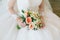 Gorgeous bouquet of white and orange flowers in the hands of the charming bide in a white dress.