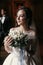 Gorgeous bride in amazing dress with bouquet and stylish groom posing at window in luxury room in hotel. rich wedding couple