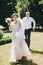 Gorgeous bride in amazing gown and stylish groom running and laughing in sunny park. Beautiful happy wedding couple enjoying time