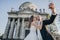 Gorgeous bride and groom taking selfie on background of old castle in park. Stylish wedding couple hugging, smiling and holding