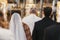 Gorgeous bride and stylish groom in golden crowns, standing with priest in church during wedding ceremony.  spiritual newlywed