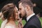 Gorgeous bride and stylish groom passionately kissing under umbrella in rainy outdoors. Sensual wedding couple embracing.