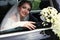 Gorgeous bride in wedding dress with bouquet of flowers posing in car