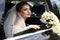 Gorgeous bride in wedding dress with bouquet of flowers posing in car