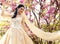 Gorgeous bride in wedding dress and crown posing in blossom summer garden