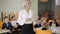 Gorgeous Caucasian teacher looking around the classroom with schoolchildren sitting at desks, and smiling at camera