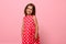 Gorgeous European baby girl, adorable child dressed in pink polka-dot dress, cute smiles posing over pink background with space