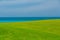 gorgeous fresh green grass field against tranquil ocean and blue sky background