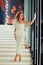 Gorgeous girl with white dress in luxury music hall standing on stairs and posing