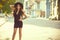 Gorgeous glam tattooed lady with long wavy hair in a little black dress and trendy fedora hat standing on the street and smiling