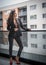 Gorgeous glamour brunette woman with black jacket posing on modern balcony with amazing view on city