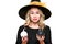 Gorgeous Halloween Witch trying to suppress laughter while holding tiny pumpkins. Cheeky woman in witches hat.