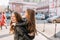 Gorgeous laughing woman posing outdoor with daughter on her back in front of cars and houses. Portrait of joyful little