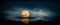 Gorgeous nighttime scene with a golden moon obscured by dark blue clouds sinking into the ocean
