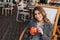 Gorgeous pale lady in good mood tasting orange cocktail in outdoor cafe. Brown-haired stylish girl in casual attire