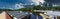 A gorgeous panoramic shot of the waterfall and the still blue lake surrounded by lush green trees with blue sky and clouds