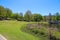 A gorgeous rippling blue lake with a brown wooden boat house on the banks surrounded by lush green trees, grass and plants